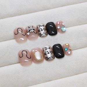 Punk style press-on nails with metal crosses, rhinestones, and lettering in a display box