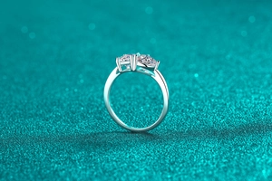 Macro shot of silver three-stone moissanite ring with emerald cut diamonds on green surface