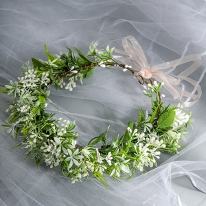 Detailed close-up of white fabric flowers and green leaves on a bridal wreath