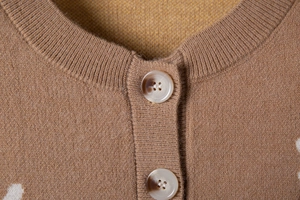 Detail of knit cardigan neckline featuring marble-patterned buttons on warm brown fabric