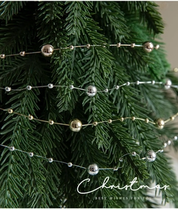 Close-up of gold and silver beaded garland layered on pine branches for Christmas decor