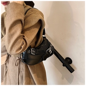 Detail of black Y2K biker shoulder bag with silver metal buckles on a model