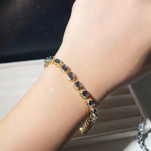 Detail shot of a gold oval blue zircon bracelet worn on a wrist under natural light