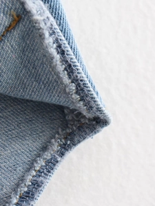 Détail macro du tissu denim bleu délavé montrant des coutures de qualité et un bord franc