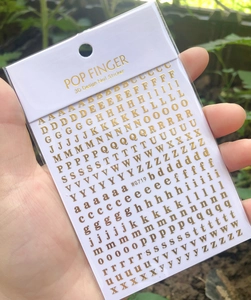 Close-up of gold 3D alphabet nail stickers in professional packaging for manicure