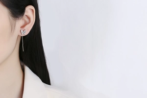 Detailed view of silver butterfly tassel earrings with zircons on a model's ear