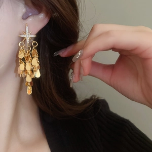 Détail des boucles d'oreilles pampilles dorées avec étoiles en zircon et gouttes d'eau