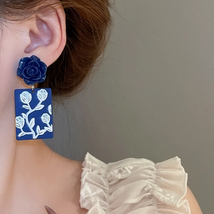 Close-up of deep blue rose earring with floral pendant worn by a model on plain background