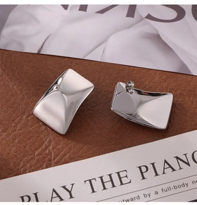 Detail showing silver curved rectangular earrings on leather and fashion magazine