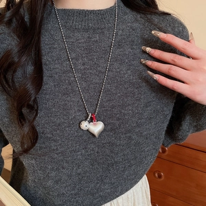 Detail of silver heart pendant and white bead on brushed bead chain with grey sweater