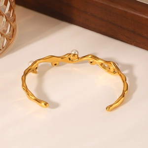 Dettaglio di un bracciale dorato a onde con perle su un espositore di gioielleria