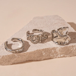 Macro detail of three irregular liquid metal silver rings on natural stone texture