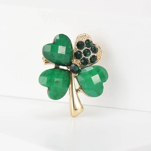 Close-up of golden four-leaf clover brooch with green crystal petals and sparkling rhinestones