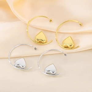Detailed view of large gold and silver hoop earrings with 3D heart pendants on silk
