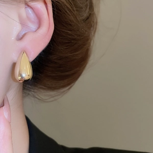 Close-up of a polished golden teardrop earring worn on a model's ear for a sleek metal look