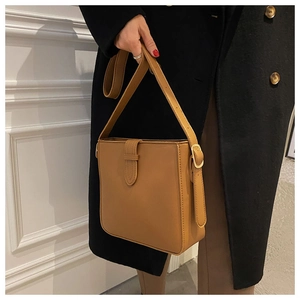 Detail of camel brown faux leather shoulder bag with adjustable strap on a black coat