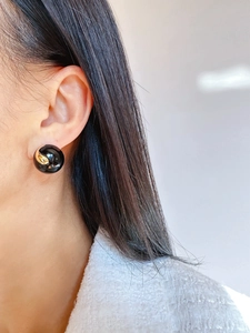 Close-up of a model wearing retro black enamel round earrings with gold swirl patterns