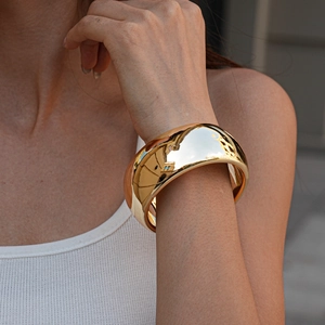 Close-up of a wide polished gold metal cuff bracelet with a mirror-like reflective finish