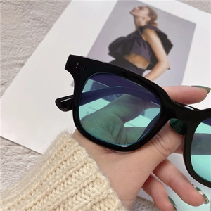Close-up of black square frame sunglasses with green lenses and silver rivet accents