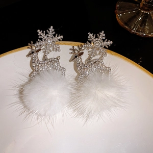 Detail of Christmas snowflake and reindeer earrings with white pompom on a ceramic plate