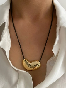 Close-up of a polished 14K gold heart pendant paired with a minimalist black cord strap