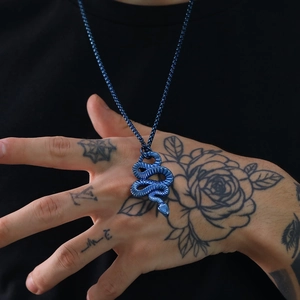 Detailed shot of blue stainless steel snake pendant necklace held by a tattooed hand