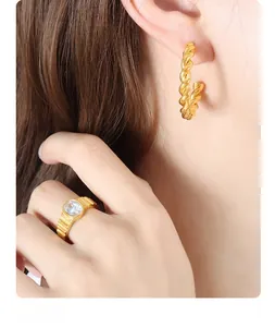 Macro detail of 18K gold twist hoop earrings and oval zircon ring on a model