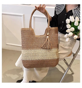 Detail of hand-woven bicolor straw bag with tassels and beads held by a model