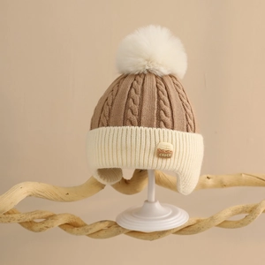 Close-up of thick cable knit texture and faux fur pompom on baby winter earflap hat