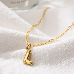 Macro shot of gold-plated 3D bubble letter L pendant necklace on white textured fabric