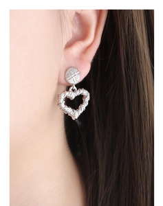 Detailed close-up of a silver-toned hollow heart earring with woven texture on a model