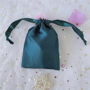 Close-up of a dark green satin drawstring pouch with silky ribbons on a starry fabric