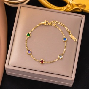 Elegant gold chain bracelet with colorful gemstones on a light brown jewelry box