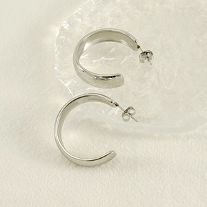 Boucles d'oreilles géométriques argentées en forme de C sur un plateau en verre chic