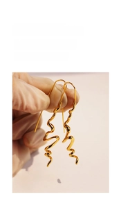 Close-up of golden spiral wave long earrings with polished mirror finish and artistic lines
