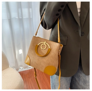 Detail of khaki bucket bag showing jacquard letter pattern and leather trim with gold hardware
