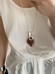 Detail shot of a large wooden teardrop pendant necklace worn on a grey sweater