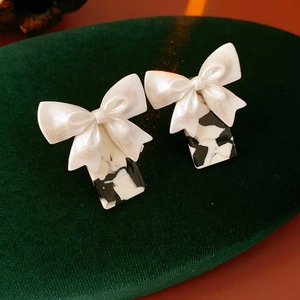 Détail de boucles d'oreilles nœud blanc avec pendentifs rectangulaires motif vache