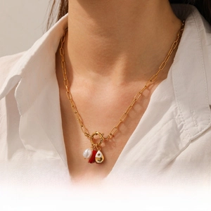 Detailed view of a gold pearl necklace featuring a red chili and blue fish pendant