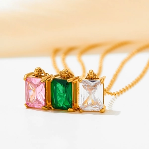 Three gold necklaces with pink, green and white zircon pendants on a soft background