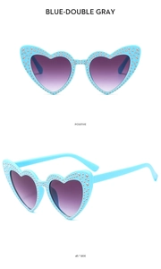 Detail view of heart-shaped sunglasses with blue rhinestone frames and purple gradient lenses