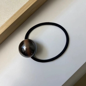 Close-up of minimalist hair tie featuring a dark brown cat-eye resin ball and black elastic