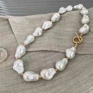 Detailed macro view of baroque pearl necklace with golden OT clasp on soft grey fabric