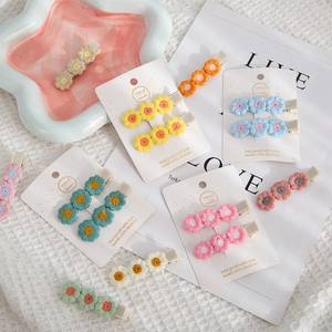 Handmade knitted daisy flower hair clips in various colors displayed on a white fabric