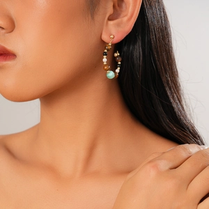 Close-up of beaded hoop earring with tiger eye and pearls worn by a model