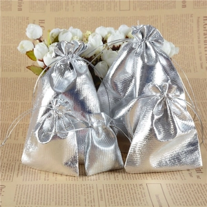 Multiple sizes of silver metallic drawstring jewelry pouches on decorative background
