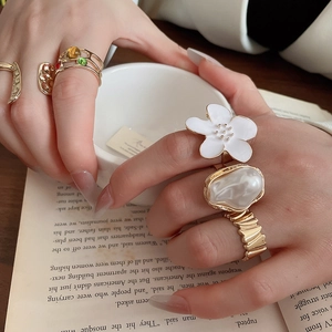 Close-up of golden ring set with floral design, colorful gems and pearl on hand