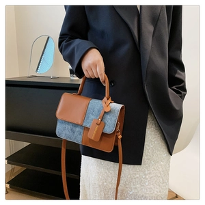 Detail of a brown leather and blue denim patchwork mini bag held by a model in a room