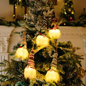 Five glowing knitted Christmas gnome ornaments with warm LED lights hanging on a tree