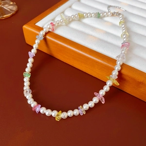 Detail of pearl necklace with colorful gemstones on white velvet jewelry display tray